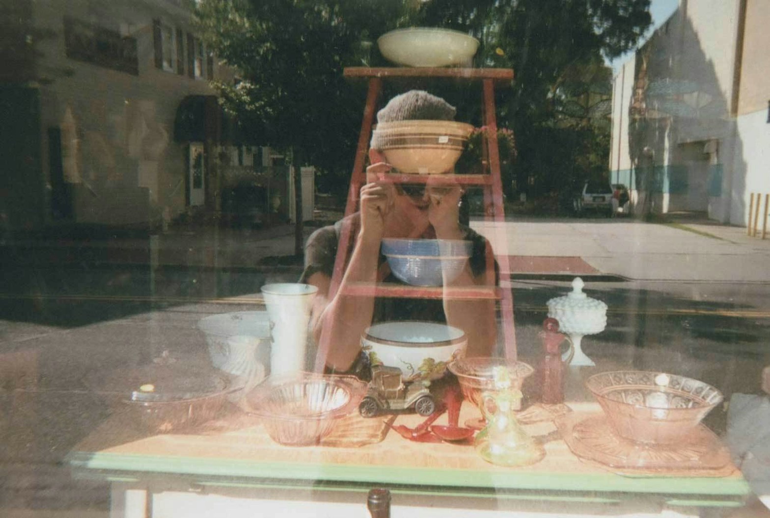 A reflection of Ted taking a photo of himself in front of a store with antique dishes in the window